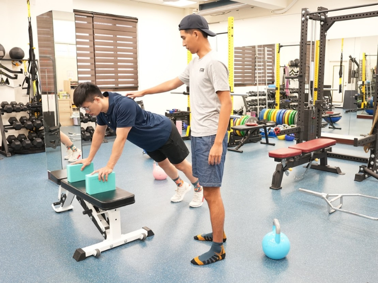唯心運動醫學體系治療師進行運動傷害恢復訓練評估，患者使用瑜珈磚在臥推凳上進行功能性訓練。